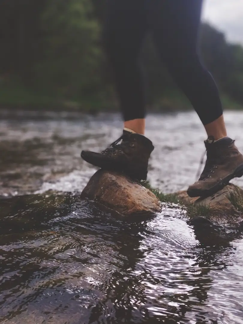 Des pieds en chaussures de randonnée traversent une rivière de pierre en pierre