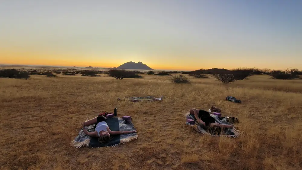 Deux personnes allongées en savasana dans les herbes dorées de la savane, au crépuscule